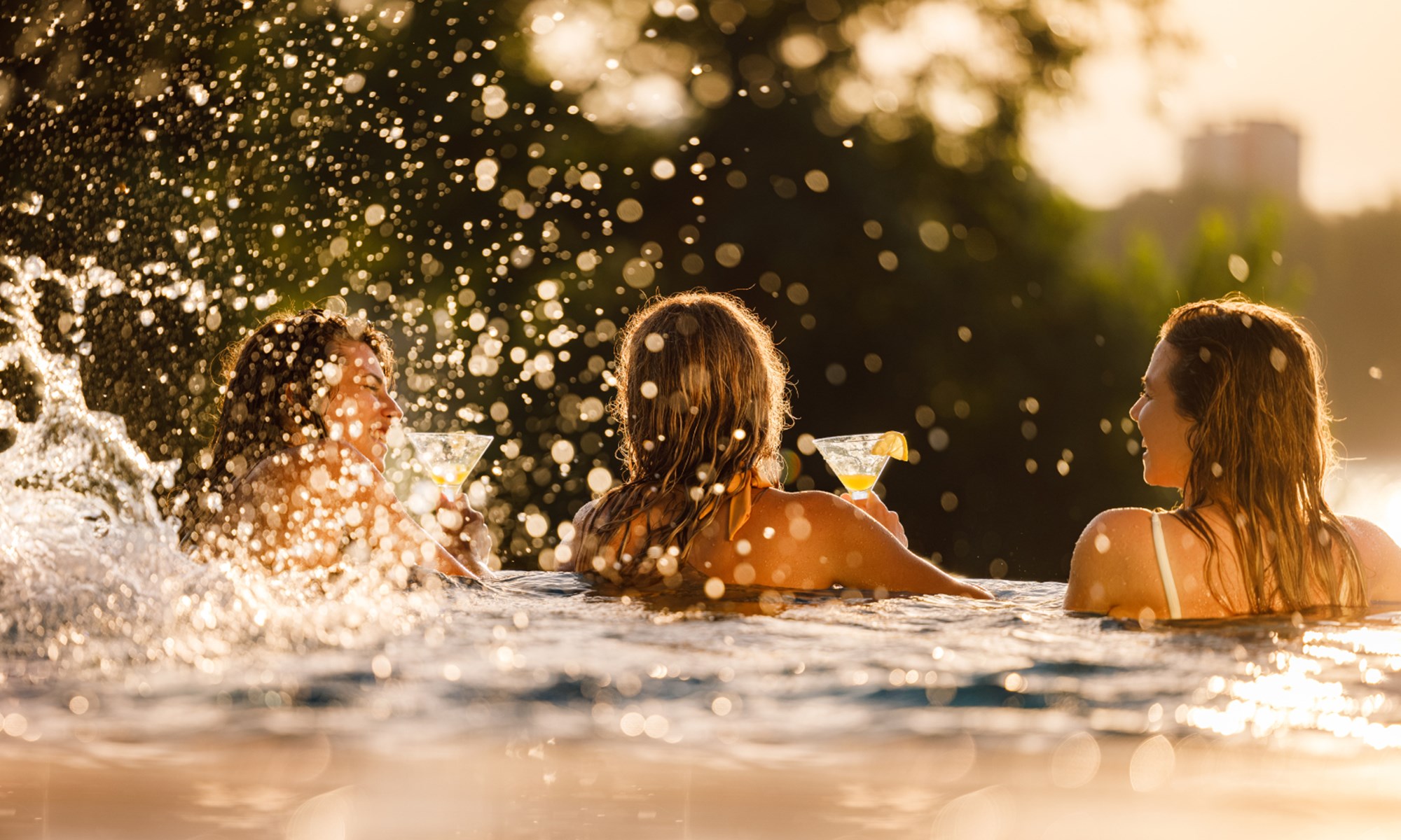 three women in pool holding cocktails splashing water